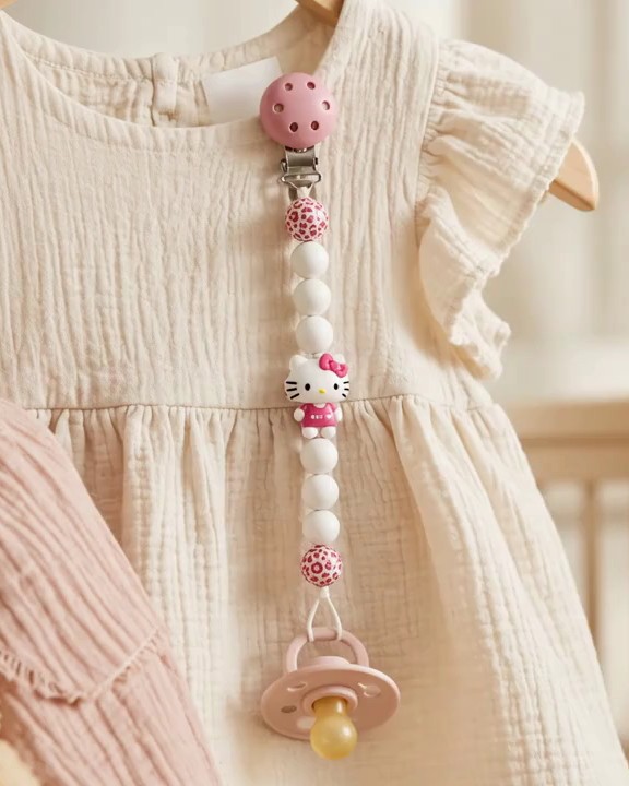 Attache-tétine personnalisée NuBaby aux perles roses et blanches, accrochée à une robe de bébé en gaze de coton crème