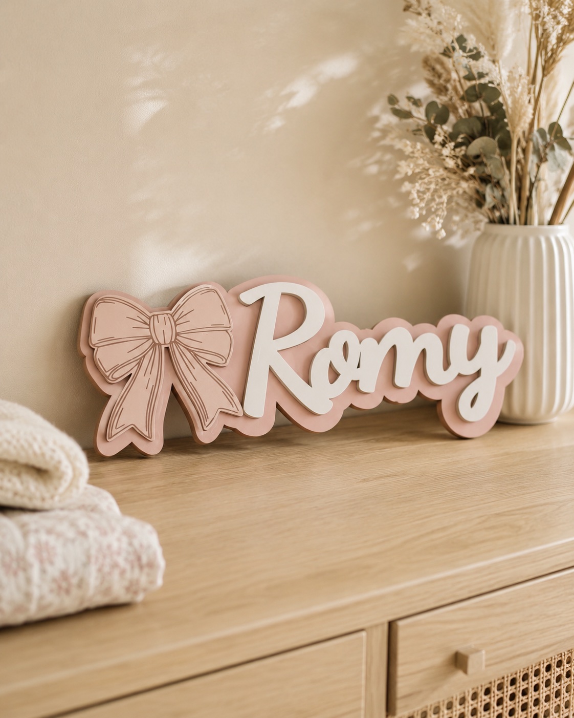Décoration murale personnalisée avec un grand nœud rose poudré, au-dessus d’un meuble d’enfant