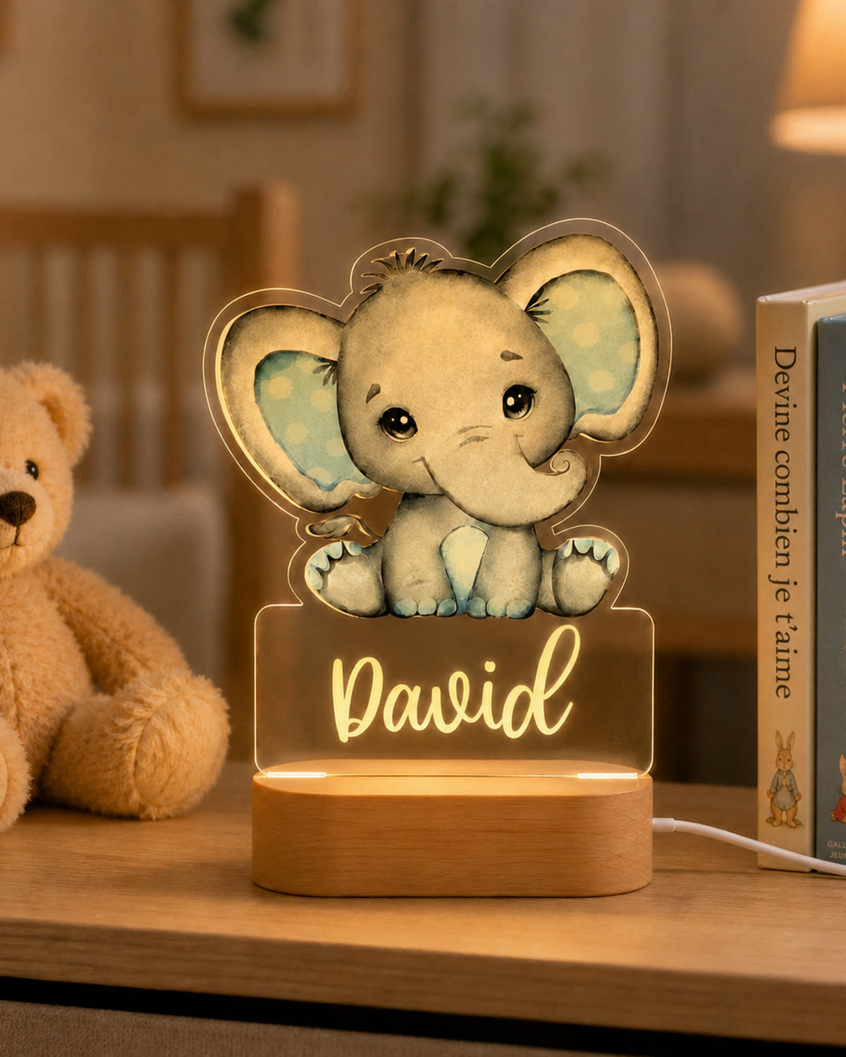 Veilleuse personnalisée Éléphant Bleu avec le prénom David, posée près de livres et d’un ours en peluche